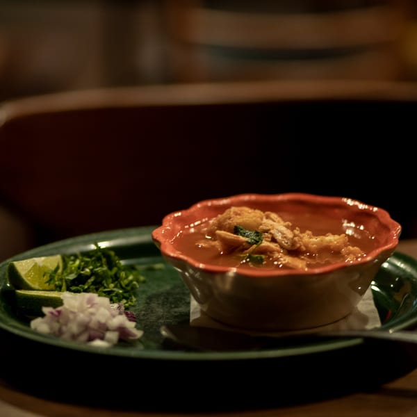 A bowl of Taxco Mexican Cuisine's chicken soup with lime, cilantro, and diced onions.