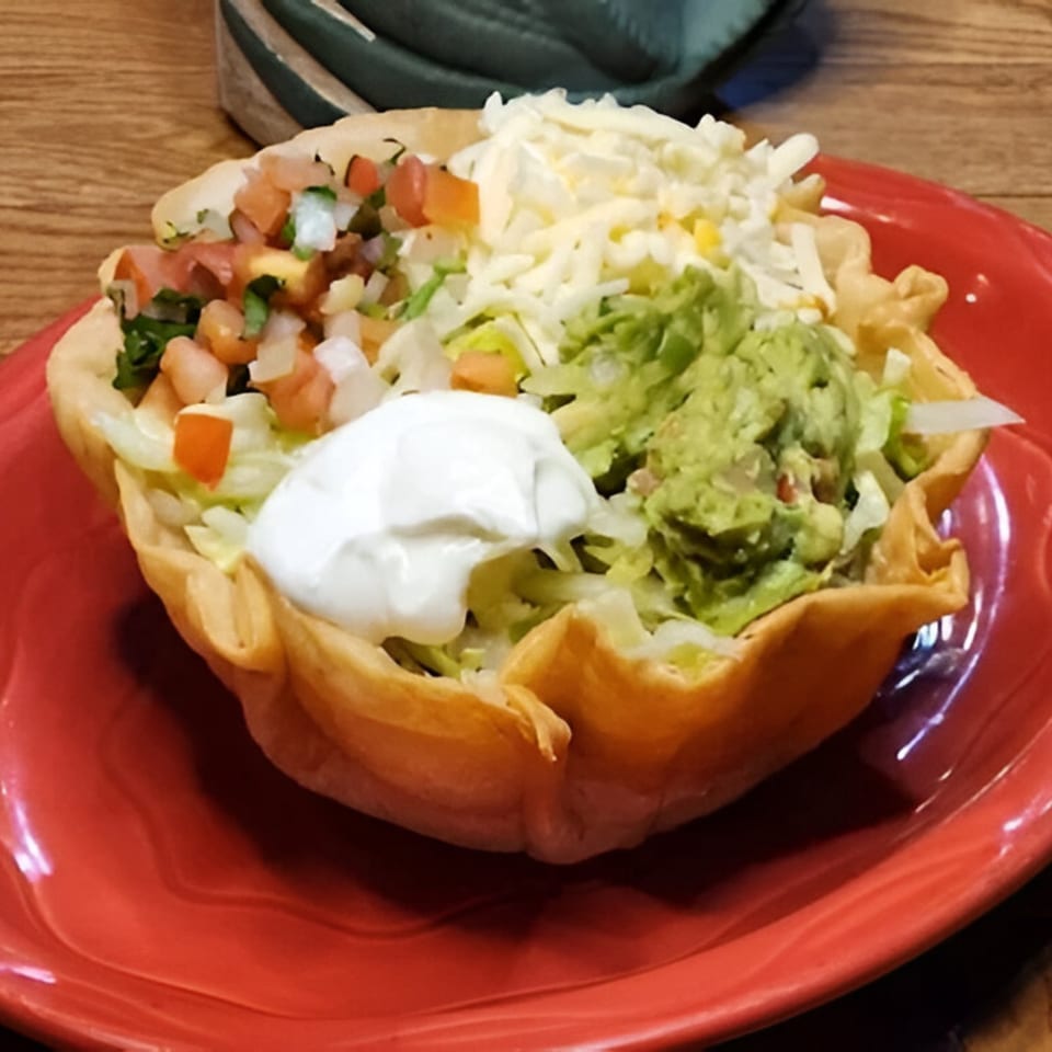 A taco salad in a crispy tortilla bowl with lettuce, pico de gallo, guacamole, cheese, and sour cream.