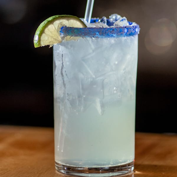Margarita with blue sugar rim, lime wedge, and straw, on a wooden table at Taxco Mexican Cuisine.