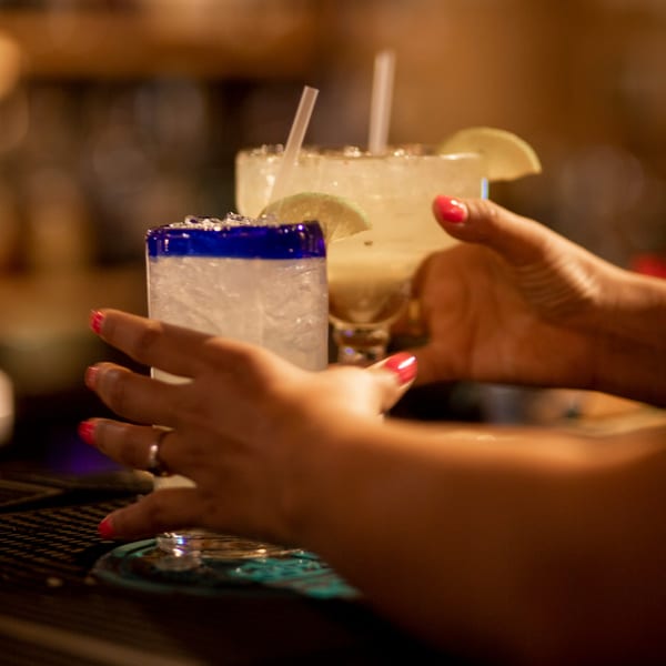 Hands with red nail polish holding two frosty margaritas with lime wedges at Taxco Mexican Cuisine.