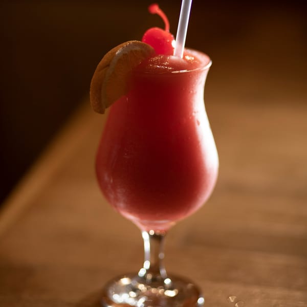 A vibrant red frozen drink in a hurricane glass, garnished with an orange slice and cherry.