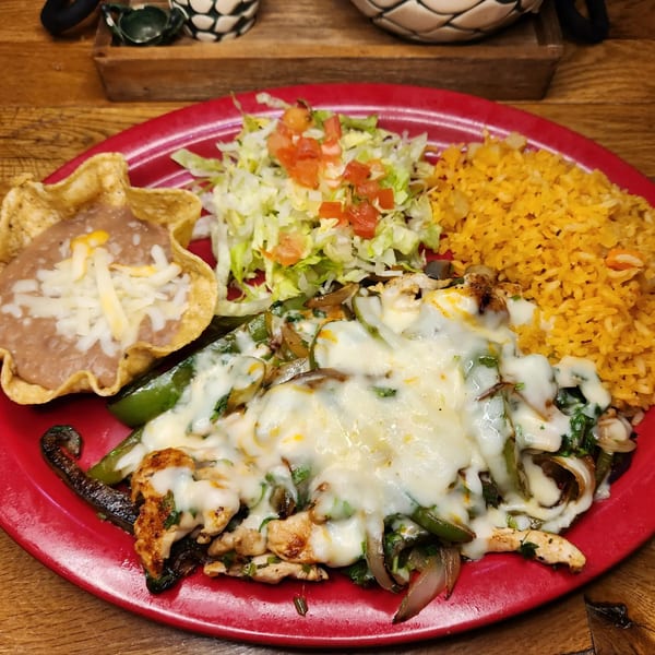 A Taxco Mexican Cuisine fajita platter with chicken, peppers, onions, melted cheese, rice, beans, and salad.
