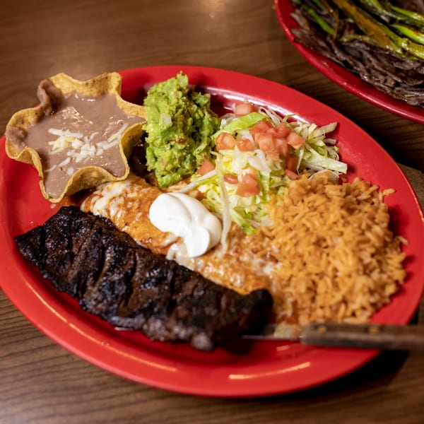 Taxco Mexican Cuisine's carne asada plate with rice, beans, guacamole, and salad on a red plate.