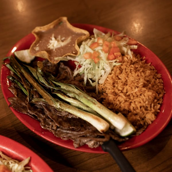 Taxco Mexican Cuisine's carne asada with grilled green onions, rice, beans, and salad on a red plate.
