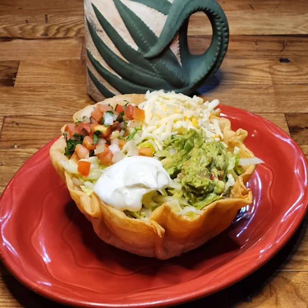 A taco salad in a crispy shell with guacamole, sour cream, pico de gallo, and cheese.