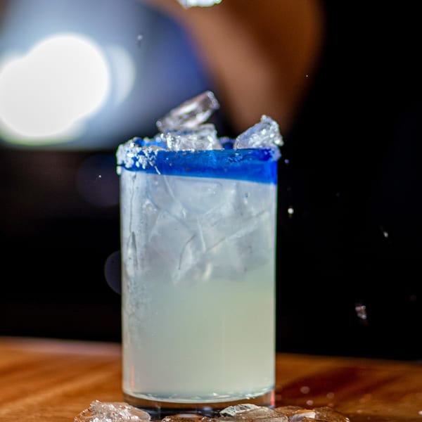 A refreshing margarita with a blue rim and ice, on a wooden surface at Taxco Mexican Cuisine.