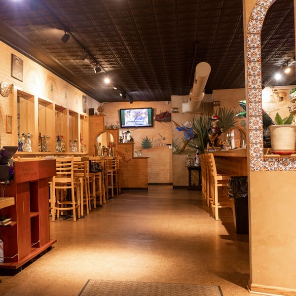 Interior of Taxco Mexican Cuisine, featuring a bar area with stools, brick walls, and Mexican-themed decor.